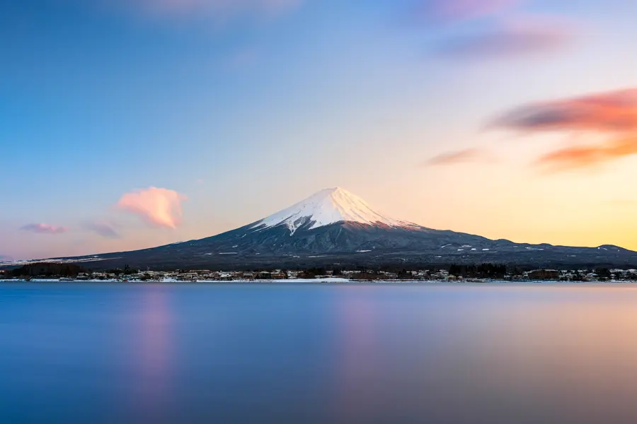 Snow-capped Mount Fuji in the evening light, a calm lake in pastel colours in front